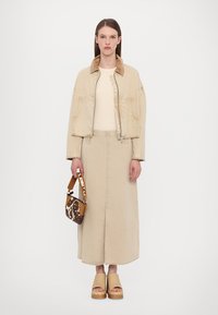 Giacca in denim beige con colletto in velluto a coste, gonna beige fino alla caviglia, borsa a tracolla motivo marrone e bianco, sandali con pianta in legno color cammello.