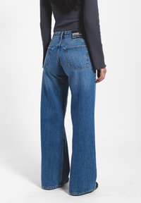 Jeans de tiro alto azules de pierna ancha en tela de mezclilla, con dos bolsillos traseros, costuras cosidas y una etiqueta de la marca en la cintura.