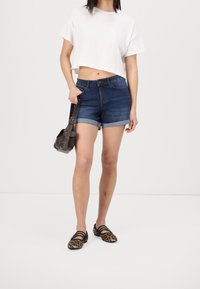 Vit kortärmad t-shirt, blå denimshorts med uppvikta kanter och svarta skor med leopardmönster. Personen håller en mörkbrun väska.