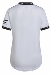 Camisa deportiva blanca de manga corta, con tejido texturizado, cuello negro con acentos rojos y blancos, y marca en la manga izquierda.