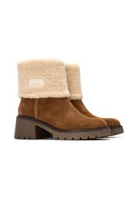 Stivali alla caviglia in suede marrone con una risvolto in shearling beige, dotati di una suola piatta spessa e texture e di un'etichetta con logo sul lato esterno.