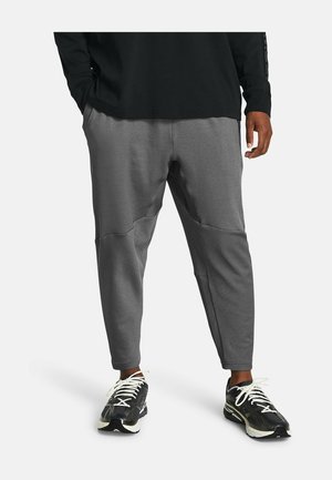 Mężczyzna ubrany w szare, teksturowane spodnie dresowe i czarne buty sportowe z białymi sznurówkami, stojący na białym tle.