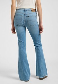 Jeans a zampa d'elefante di colore azzurro chiaro in denim, con tasche posteriori e un'etichetta "Lee" marrone in vita. Presentano una texture liscia e una vestibilità casual.
