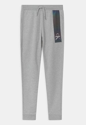 Hellgraue Jogginghose mit gerippten Bündchen, Kordelzug in der Taille, Seitentaschen und einem vertikalen schwarzen Calvin Klein Jeans-Logo am rechten Oberschenkel.