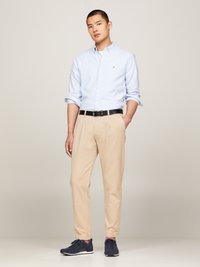 Camisa de botão azul clara com riscas, calças bege, cinto preto, ténis azul-marinho. Tecido suave, corte ajustado e mangas arregaçadas.