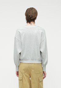 Svetlošedý mikina s posadenými ramenami a rebrovanými manžetami. Má okrúhly výstrih a jemnú textúru, kombinovanú s béžovými cargo nohavicami.