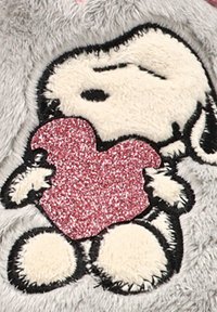 Snoopy sosteniendo un corazón rojo brillante sobre un fondo de tela gris suave y texturizada.