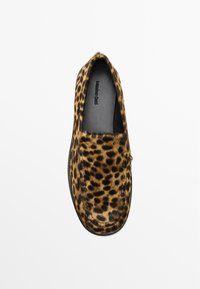 Chaussure à enfiler en imprimé léopard, fabriquée en fourrure douce avec une semelle plate. Présente un bout rond et des détails cousus le long des coutures.