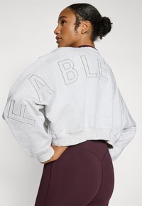 Grå kort sweatshirt med oversized tekst "FABLE" på ryggen, med ribbede mansjetter og en myk tekstur. Kombinert med bordeaux leggings.