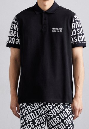 Camisa polo de algodón negro, con mangas cortas blancas de patrón contrastante y texto de logotipo. Detalles de textura en la tela.