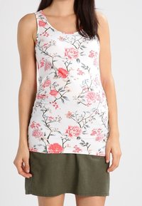 Top sin mangas floral con base blanca que presenta flores en tonos rosa y rojo. Combinado con una falda corta de un verde oscuro, el tejido parece suave y ligero.