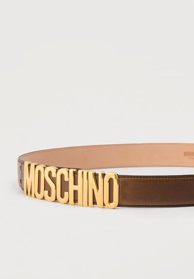 Καφέ δερμάτινη ζώνη με μεγάλα χρυσά γράμματα που σχηματίζουν τη λέξη "MOSCHINO" ως το κύριο στοιχείο της αγκράφας, πάνω σε απλό φόντο.