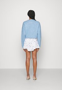 Pulôver azul de malha e saia branca com padrão floral, com comprimento curto, apresentando um leve babado. Tecido leve e texturizado com um corte descontraído.