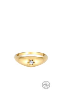 Anello in metallo dorato con una banda liscia e arrotondata. Presenta una struttura a stella ben visibile con un cristallo trasparente al centro.