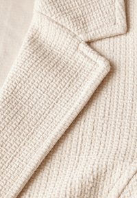 Kermanvaaleabråiden kangas, jossa on tekstuuri ja kudottu kuvio sekä terävät läpät. Kangas vaikuttaa pehmeältä ja hieman kohotetulta, mikä antaa syvyyttä.