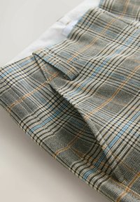 Plaid fabric swatch in beige, blue, and brown tones. Features a textured weave with visible lines and patterns throughout.