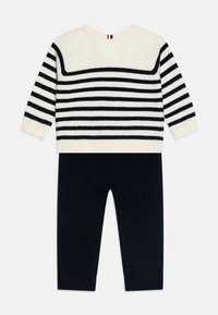 Pull rayé crème et marine, à manches longues, tricot texturé et poignets côtelés, associé à un pantalon en maille marine, ajusté aux chevilles.