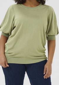 Lichtgroene trui met korte mouwen en een losse pasvorm, geribbelde boorden aan de mouwen en zoom. Zachte textuur met een lichte glans, geschikt voor casual gebruik.