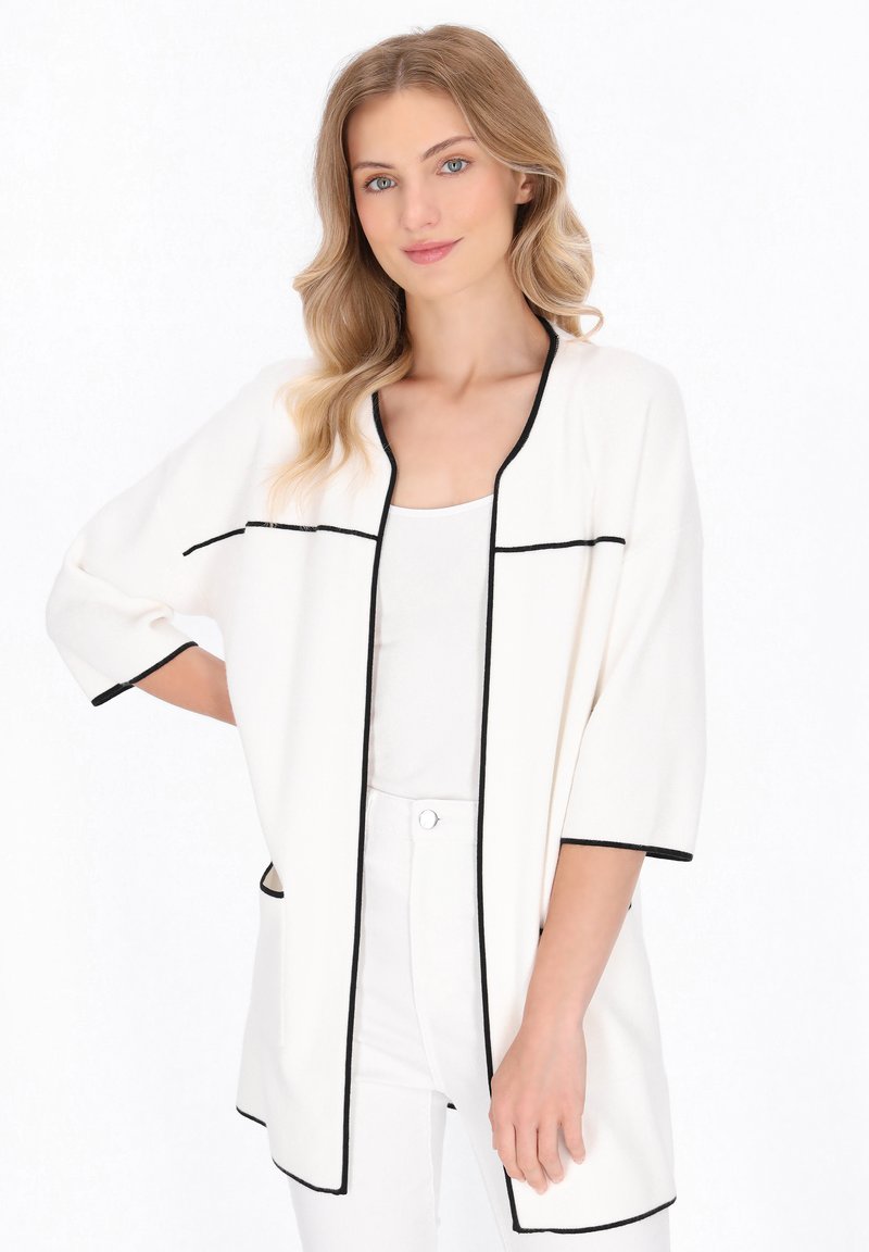 Lichtgewicht witte cardigan met zwarte bies, open voorkant, korte mouwen en zijzakken, gecombineerd met een witte top en broek.