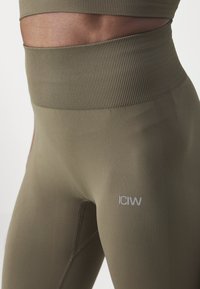 Leggings taille haute vert olive en matière extensible, avec une texture côtelée à la taille et un petit logo blanc sur la cuisse.