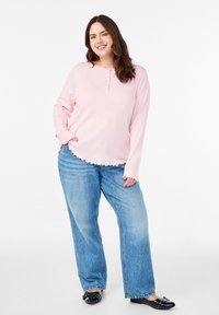 Šviesiai rožinė ilgarankovė palaidinė su mygtukų akcentais, išilgine apatine dalimi, derinama su aukštu liemeniu mėlynomis plačiomis kelnėmis ir juodais plokščiais batais.