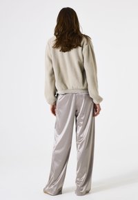 Chaqueta de forro polar gris claro con textura suave, combinada con pantalones de satén gris claro brillantes. Corte sencillo y relajado con cinturilla elástica.