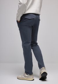 Pantalones ajustados de color azul oscuro con bolsillos traseros, textura suave y un ligero estiramiento. Combinados con zapatillas gris claro que presentan una suela en contraste.