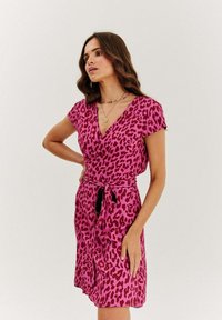 Ružová leopardí potlač šiat s krátkymi rukávmi, výstrihom do V a viazaním v páse. Tkanina vyzerá hladko s jemným leskom.