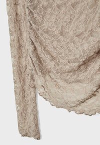 Blonde sjal i en blød beige farve, med intrikate blomster mønstre, bølgede kanter og et draperet design. Let og struktureret stof.