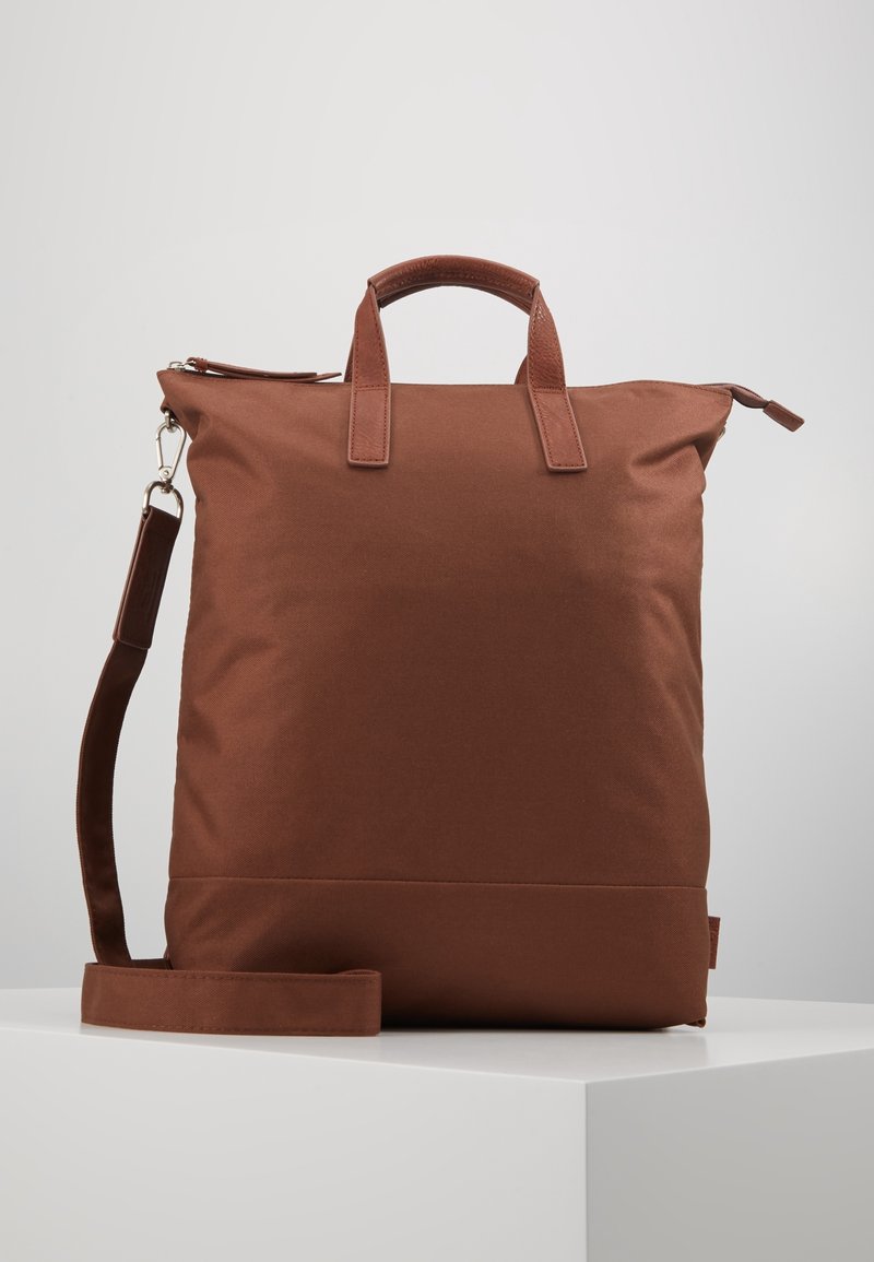 Brown fabric backpack with two top handles and a detachable shoulder strap. Smooth texture with a zip closure and minimalistic design.