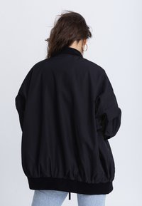 Veste bomber noire à coupe ample, avec un ourlet élastiqué et des poignets élastiques. Finition lisse, détails matelassés le long des coutures.