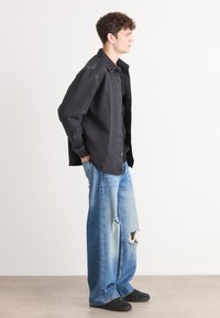 Black denim button-up shirt, relaxed fit; paired with light blue, distressed wide-leg jeans featuring rips; casual black shoes.