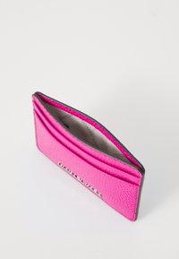 Różowy, teksturowany portfel na karty z wieloma slotami i kontrastującą szaro-brzegowaną krawędzią, z delikatnym logo w kolorze srebrnym. Otwiera się na jasne wnętrze.