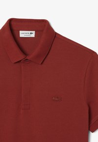 Röd polo-t-shirt i texturerat tyg, med klassisk krage, en enkel knappslå och en broderad logotyp på bröstet.