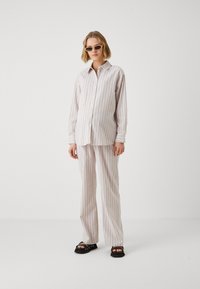 Lahka pajama komplet s črtami v umirjenih tonih, ki vključuje srajco na gumb in hlače sproščenega kroja. Okrašen z ovratnikom in manšetami.