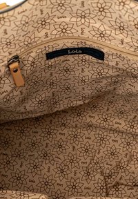 Interior beige de un bolso con un patrón floral en marrón oscuro. Incluye un bolsillo con cremallera y una etiqueta de la marca con la inscripción "Lois".