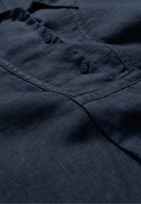 Diepblauwe linnen blouse met een knoopsluiting, subtiele textuur en een ontspannen kraag. Bevat vier afgeronde knopen en nette stiksels.
