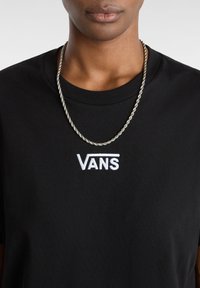Sort bomuld t-shirt med et hvidt broderet "VANS"-logo. Bæres med en snoet sølvkæde-halskæde. Enkel rund halsudskæring og korte ærmer.