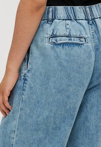 Lyseblå denimjeans har en avslappet passform, elastisk midjebånd og en baklomme med kontrasterende søm. Stoffoverflaten er glatt.