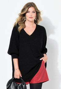 Czarny sweter z dzianiny z dekoltem w kształcie V i oversize'owymi rękawami, zestawiony z czerwoną skórzaną mini spódnicą i czarną torebką. Tekstura jest prążkowana.