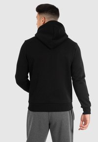 Sweat à capuche noir avec une poche kangourou, des poignets et un ourlet côtelés. Comprend une capuche avec cordon de serrage et un tissu doux, associé à un pantalon de survêtement gris.