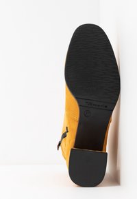 Bottine en daim jaune avec une semelle en caoutchouc noir texturé. Présente une fermeture éclair sur le côté et un design minimaliste. Taille 37 indiquée sur le talon.
