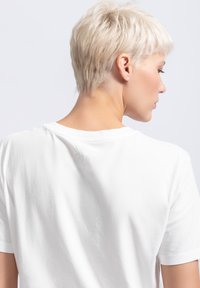Witte katoenen t-shirt met korte mouwen, voorzien van een ronde hals en een subtiele geborduurde detail nabij de achterkant van de halslijn. Gladde textuur.