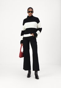 Maglione lavorato a maglia spesso a righe bianche e nere con collo alto, abbinato a pantaloni neri a zampa, stivali neri alla caviglia e una borsa rossa.