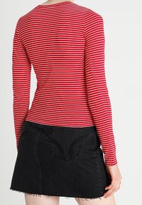 Röd och vit randig långärmad topp som matchas med en svart denimminikjol. Kjolen har en fransad nederkant och bakfickor.