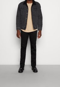 Svart denimjacka med Sherpa-krage, beige t-shirt, svarta byxor och svarta sneakers. Enkel design, typisk passform och synliga sömnadsdetaljer.