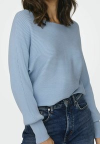 Light blue ribbed sweater with a wide neckline and slightly puffed long sleeves, paired with dark denim jeans.