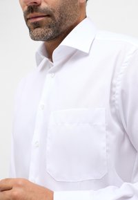 Camicia da uomo in cotone bianco con colletto classico, tasca singola e chiusura a bottoni. Texture liscia con vestibilità su misura.