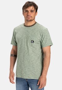 Vihreä raidallinen lyhythihainen t-paita pyöreällä kaula-aukolla, jossa on tasku, jossa on logopatch. Pehmeä puuvillakangas ja rento istuvuus.