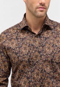 Camicia marrone con motivo paisley in oro, blu e bordeaux. Presenta un colletto aperto e dettagli con bottoni sul davanti.